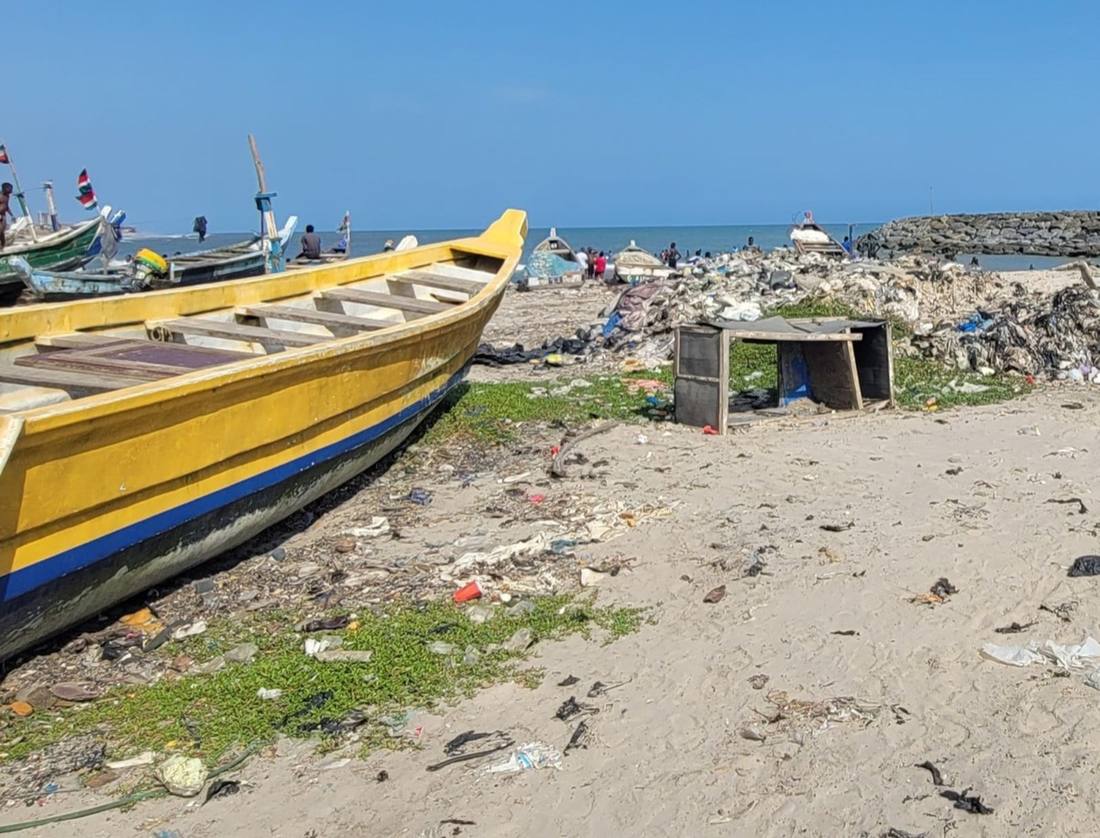 Fishing boat beside a large pile of plastic waste on a Ghanaian beach