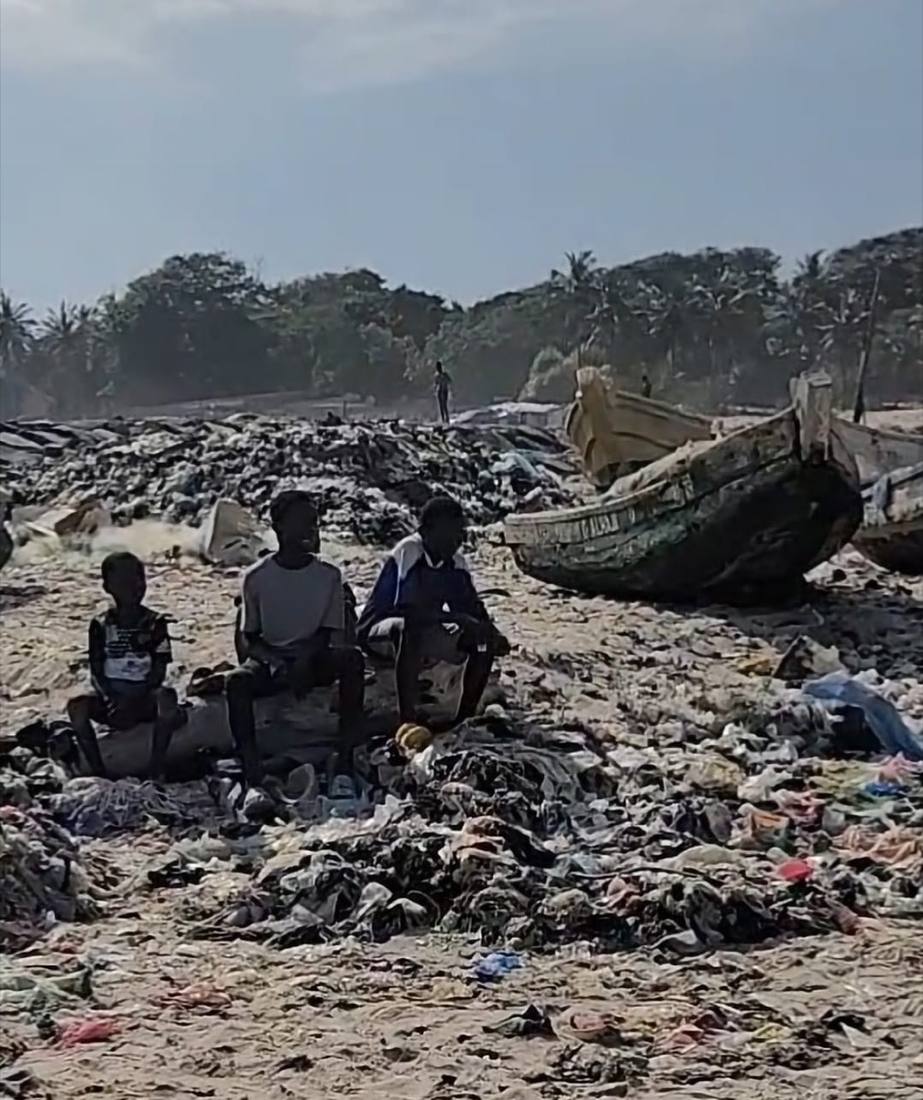 Children sitting among accumulated plastic waste near fishing boats in Ghana